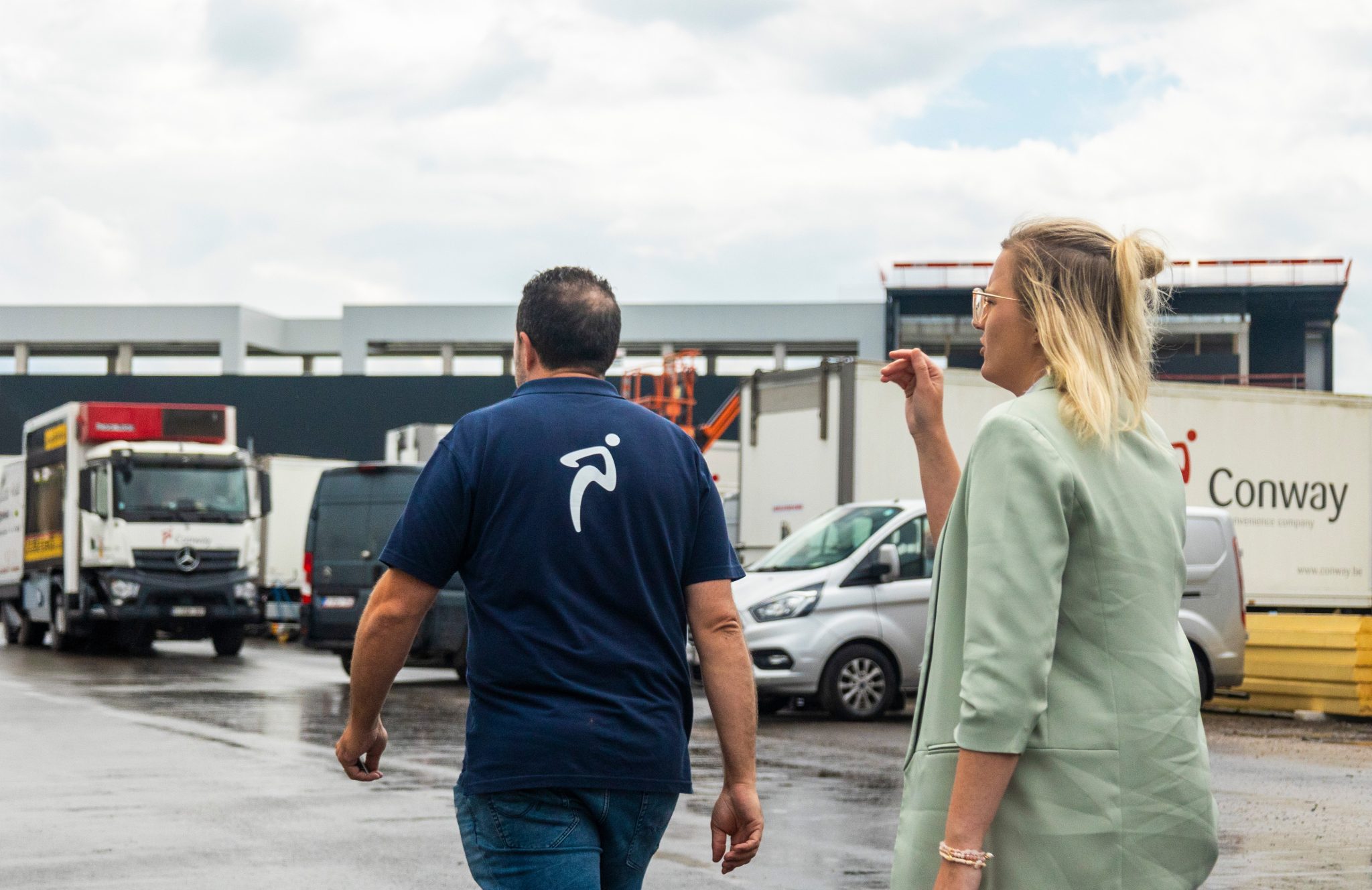 Des employés de Conway au dépôt, avec un camion frigorifique de l'entreprise, des fourgonnettes et une semi-remorque derrière eux.