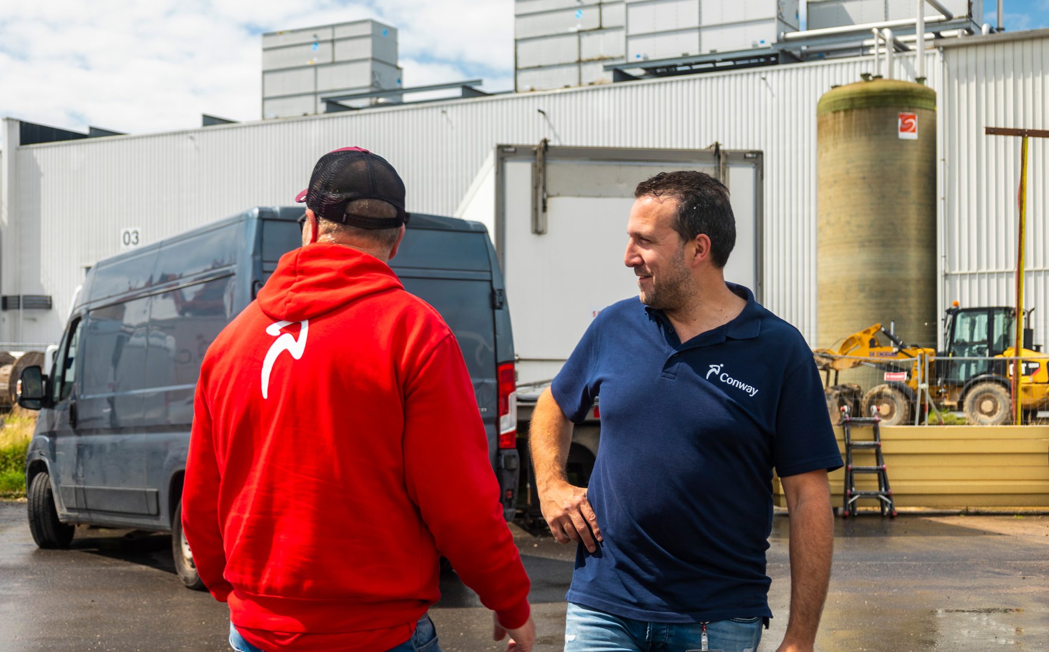 Deux employés de Conway discutent au dépôt, à côté d'une camionnette de livraison et d'une remorque frigorifique.
